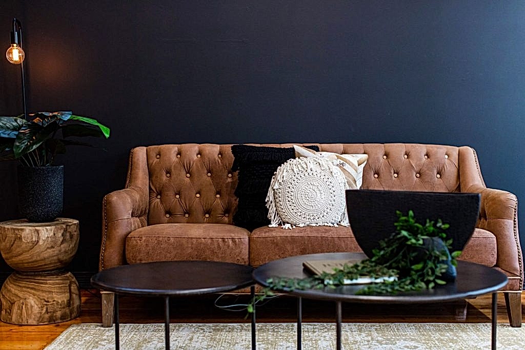 Two round coffee tables in front of brown leather lounge with brown and white pillows